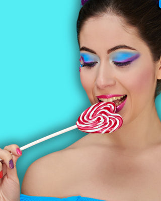 Frau ist einen Dauerlutscher Lollipop und tragt bunte Farben. Hier gelangst du zur Kategorie DRACHEN-DILDO.