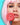 Frau mit rosa schulterlangen Haaren die in ihrer rechten Hand einen großen runden Dauerlutscher an ihre leicht geöffneten Lippen hält