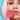 Frau mit rosa schulterlangen Haaren die in ihrer rechten Hand einen großen runden Dauerlutscher an ihre leicht geöffneten Lippen hält